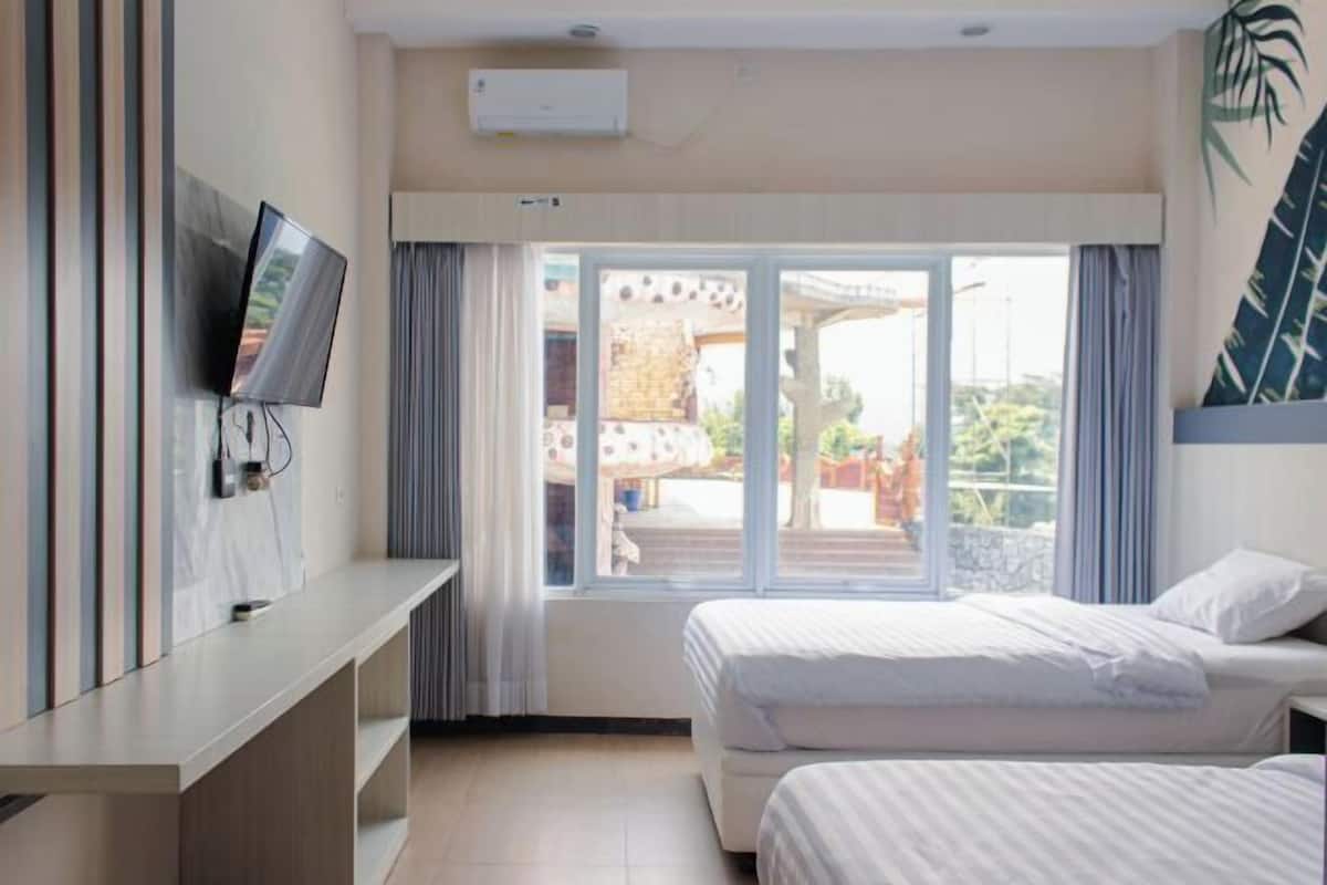 Habitación de hotel con dos camas, un televisor sobre un mueble bajo, un ventanal con cortinas y vistas al exterior.