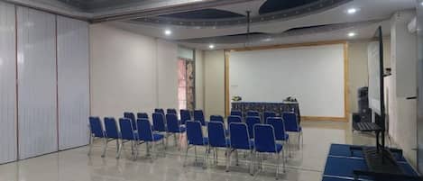 A conference room with rows of blue chairs, a whiteboard, and a projection screen.
