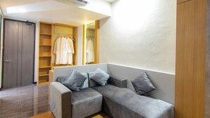 Una sala moderna con un sofá seccional gris, un armario de madera y un armario empotrado con ropa colgada.