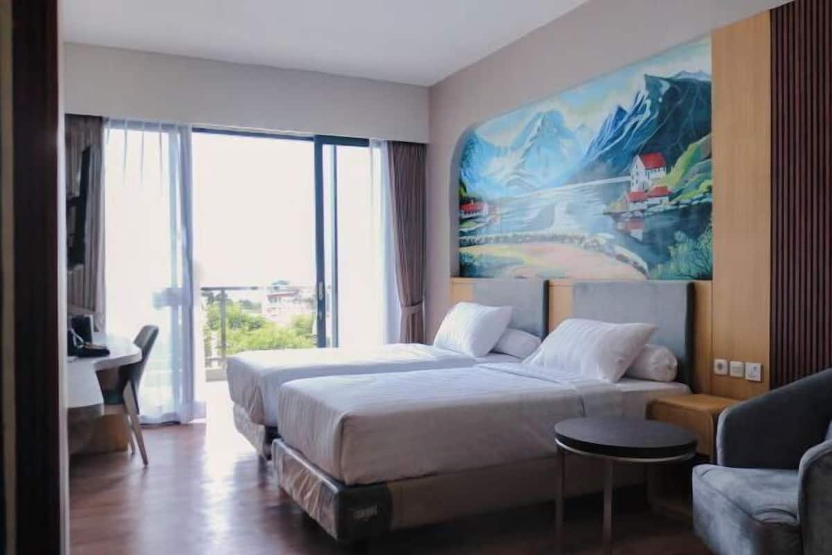 Una habitación de hotel con cama, escritorio, silla, una mesita y un cuadro en la pared.