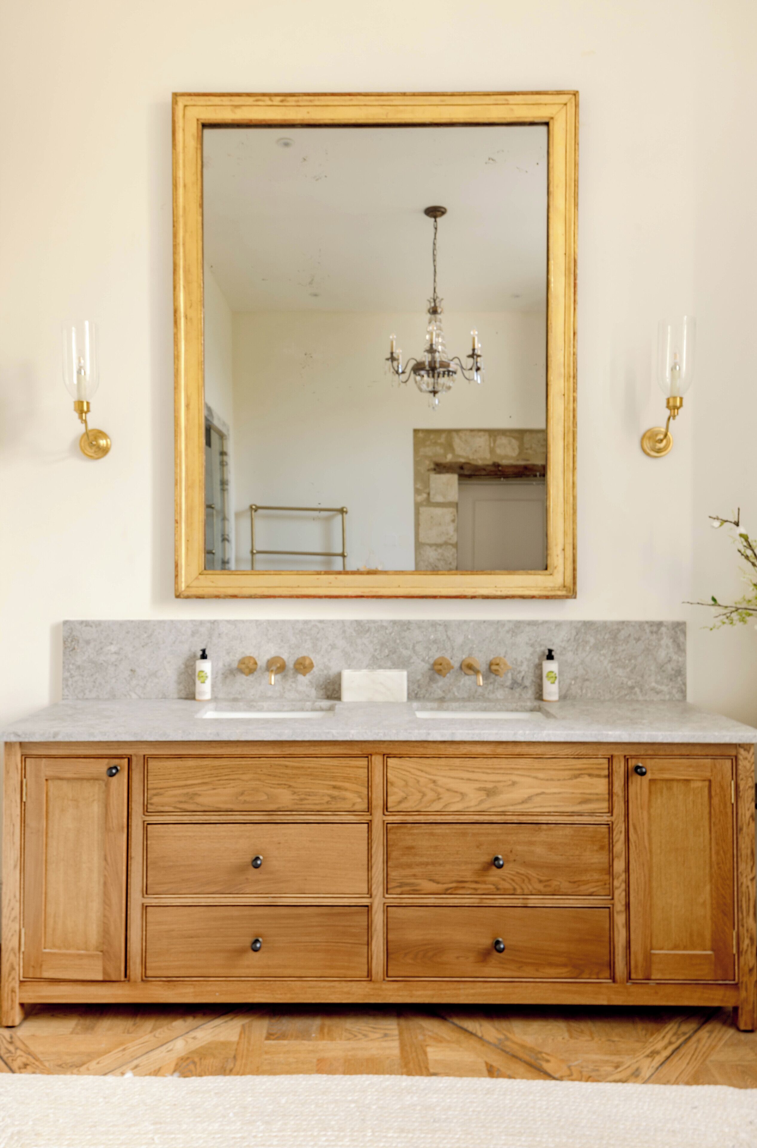 A bathroom with a wooden vanity, a large mirror, and a chandelier.