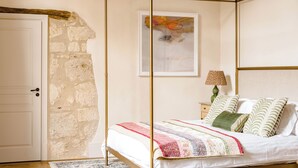 Ein Schlafzimmer mit Himmelbett, Steinwand, gerahmtem Kunstwerk, Nachttisch mit Lampe und einer Tür.