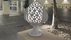 A modern outdoor lamp with a geometric design, placed on a concrete base near a palm tree. - ONDA BIANCA LUXURY APARTMENTS (Realmonte)