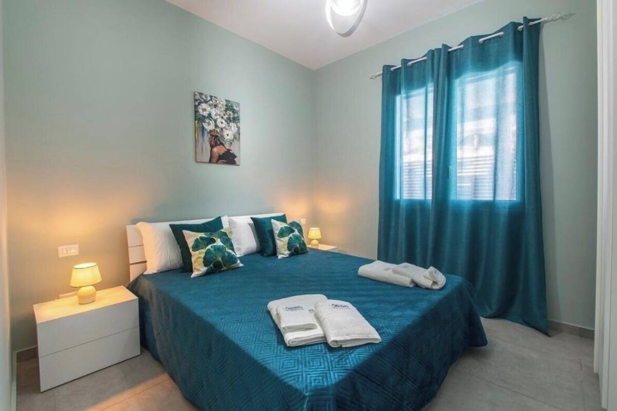 A bedroom with a bed, pillows, a nightstand, a lamp, and a window with curtains.