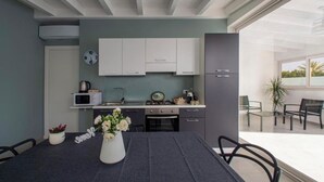 A modern kitchen with white cabinets, a dining table with a vase of flowers, and a view of the outdoor patio area. - ONDA BIANCA LUXURY APARTMENTS (Realmonte)