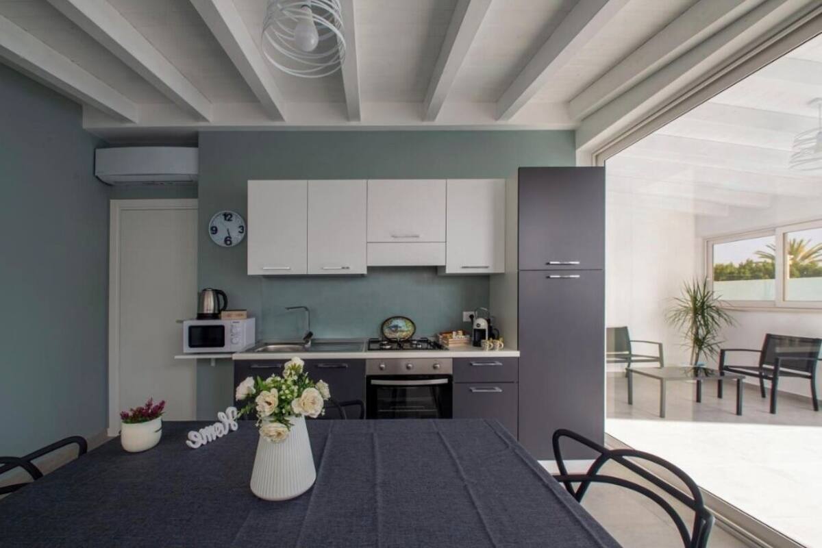 A modern kitchen with white cabinets, a dining table with a vase of flowers, and a view of the outdoor patio area.