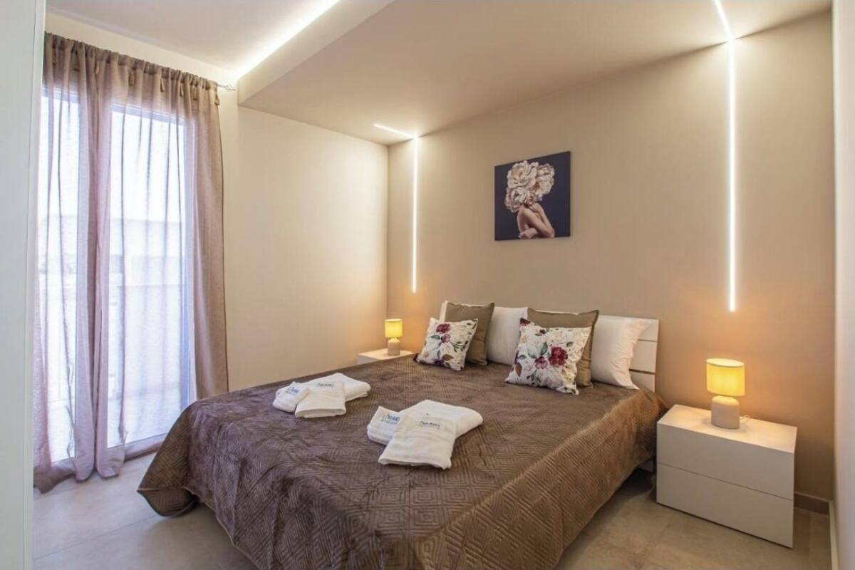 A hotel room with a large bed, two bedside tables with lamps, a window with curtains, and a wall-mounted picture.