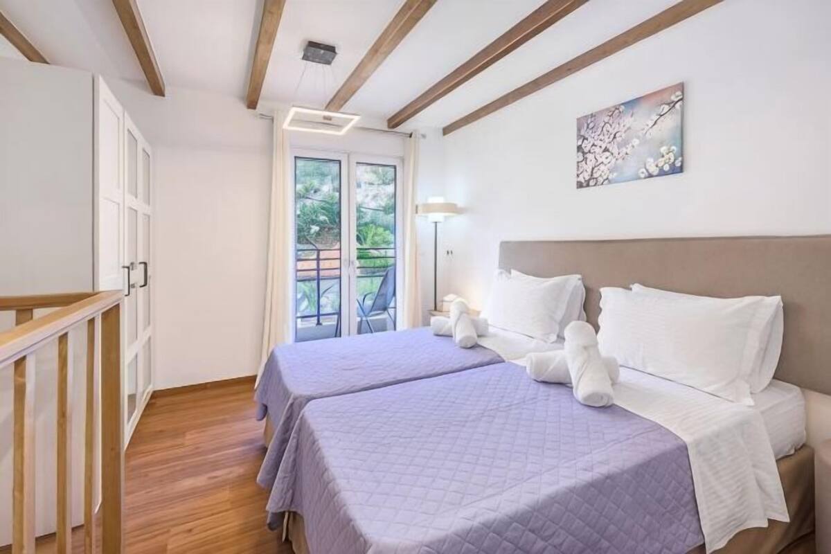 A bedroom with two beds, a balcony, and a painting on the wall.