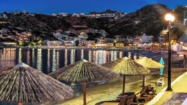 A beach with thatched umbrellas and lounge chairs, a calm sea, and buildings on a hillside in the background. - BlueGreen Holiday Homes: Holidays with Seaview (Malevizi)