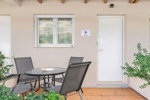 Un patio con una mesa redonda y cuatro sillas, una puerta blanca y una ventana con vistas a zonas verdes.