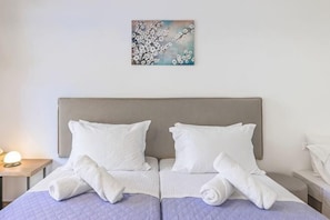 A double bed with white linens and towels, a headboard, and a painting on the wall. - BlueGreen Holiday Homes: Holidays with Seaview (Malevizi)