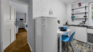 A modern kitchen with white cabinetry, a white refrigerator, a dining table with blue chairs, and a patterned tile floor.