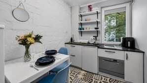 A compact kitchen with white cabinets, a dining table with chairs, a window with a view of greenery, and a small countertop with a coffee maker.