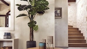 A modern interior with a round wooden table, a large potted plant, wicker baskets, and a staircase against a textured wall. - Casa Di Pietra - Four Bedroom Villa, Sleeps 8 (Zakynthos)