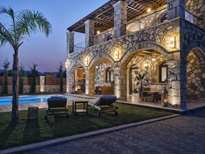 A stone-clad house with a pool, outdoor seating, and a well-lit interior. - Casa Di Pietra - Four Bedroom Villa, Sleeps 8 (Zakynthos)