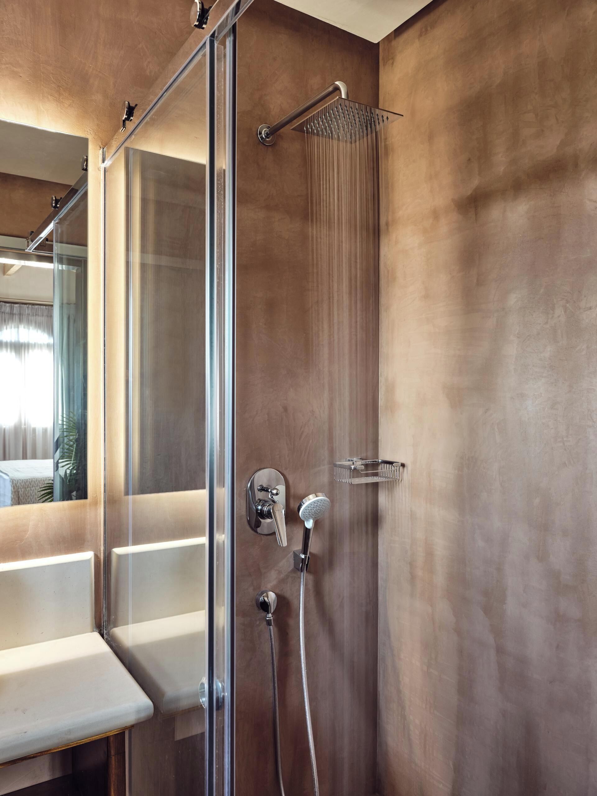 A modern bathroom with a glass shower enclosure, a handheld showerhead, and a wall-mounted faucet.