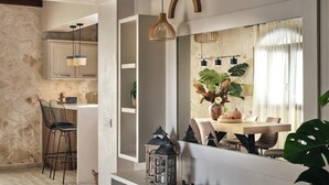 A modern kitchen with a stone wall, bar stools, pendant lights, and a dining area with a table, chairs, and plants. - Casa Di Pietra - Four Bedroom Villa, Sleeps 8 (Zakynthos)