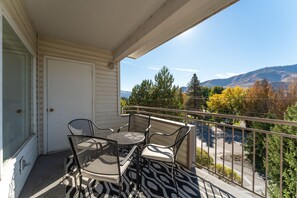 Un balcon avec une table et des chaises, une vue sur les arbres et les montagnes, et une porte blanche.