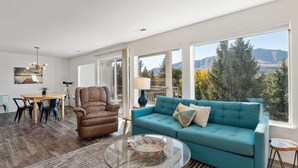 A spacious living room with a large window, a blue sofa, a brown armchair, and a glass coffee table. - Modern Park Point - Walk to Town (Chelan)