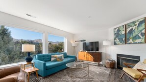 A modern living room with a blue sofa, a brown leather couch, a glass coffee table, and a fireplace. - Modern Park Point - Walk to Town (Chelan)