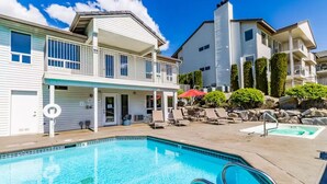 A swimming pool area with lounge chairs and a red umbrella, surrounded by buildings with balconies and a clear blue sky. - Modern Park Point - Walk to Town (Chelan)