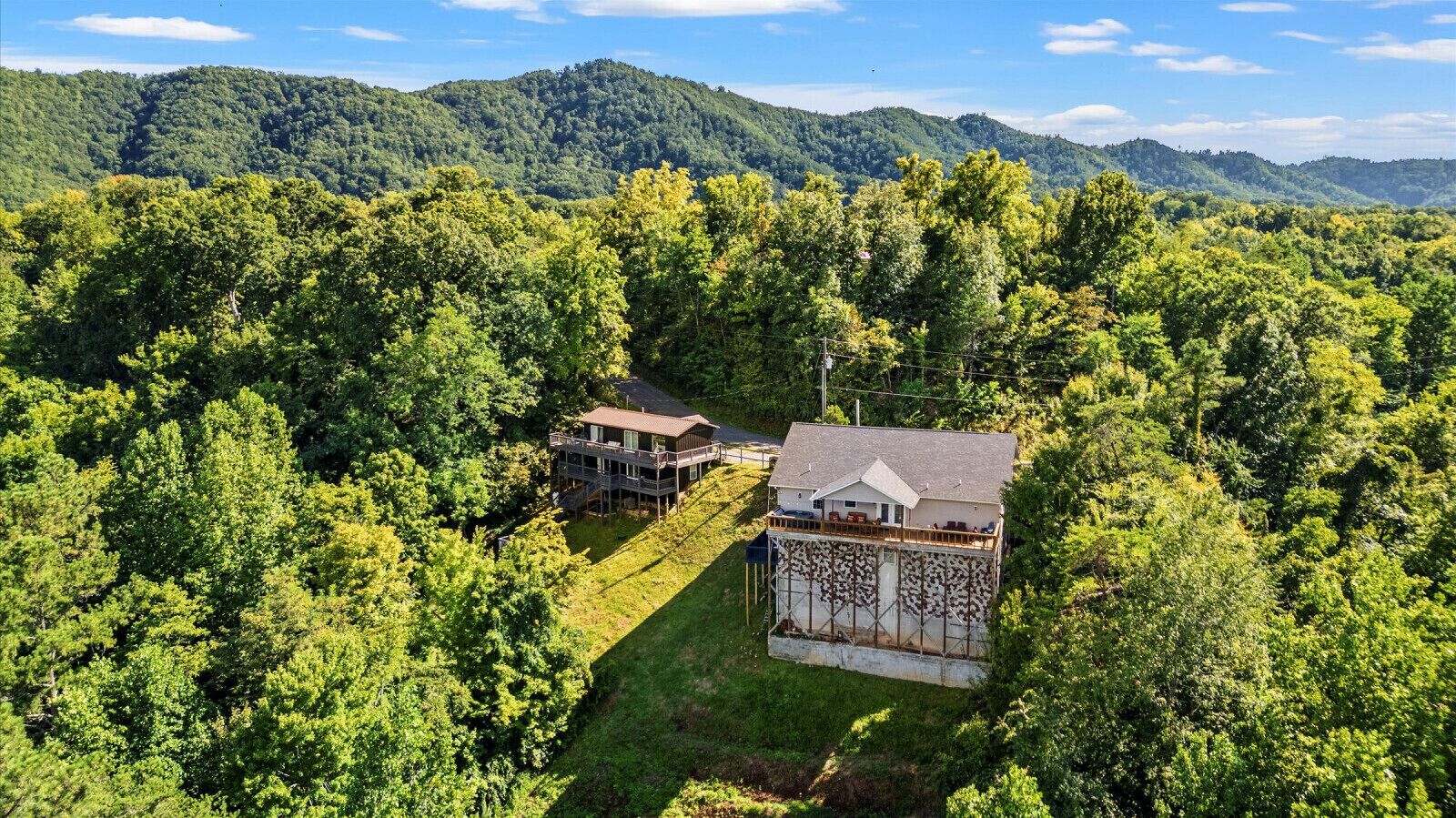Une maison à deux étages dotée d’un balcon, entourée d’une forêt dense et avec des collines en arrière-plan.