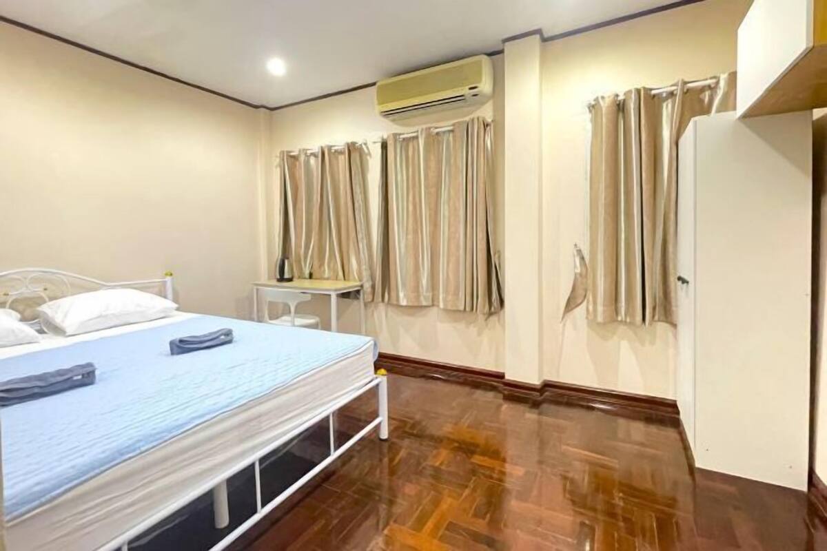 A hotel room with a bed, a desk, an air conditioner, and curtains.