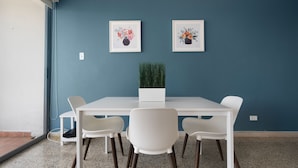 A room with a white table and four white chairs, two framed floral artworks on the wall, and a potted plant on the table. - Coastal Charm Panoramic Scenes Direct Shorelin (San Juan)