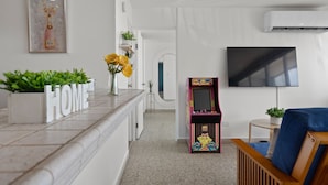 A modern living room with a marble countertop, a framed artwork, a flat-screen TV, and a retro arcade game. - Coastal Charm Panoramic Scenes Direct Shorelin (San Juan)