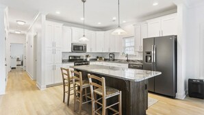 Une cuisine moderne avec des meubles blancs, un grand îlot central doté de tabourets, des appareils en acier inoxydable et un éclairage suspendu.