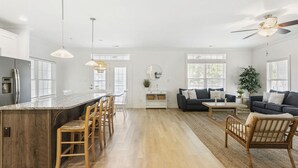 Un vaste espace de vie comprenant une grande table à manger en bois, un canapé bleu foncé et un ventilateur de plafond.