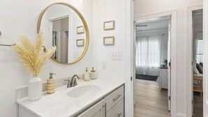Une salle de bain moderne avec un grand miroir, deux lavabos et un vase contenant des fleurs séchées.