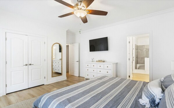 Quarto com cama, ventoinha no teto, penteadeira, espelho e chuveiro.