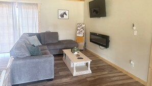 A living room with a grey sofa, a white coffee table, and a TV mounted on the wall. - Wild Horses/ Scenic Ranch Retreat (Bucyrus)