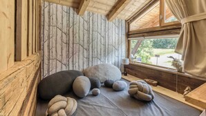 A cozy room with a wooden ceiling, a window with curtains, and a wall with a tree pattern.