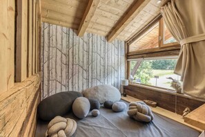 A cozy room with a wooden ceiling, a window with curtains, and a wall with a tree pattern.