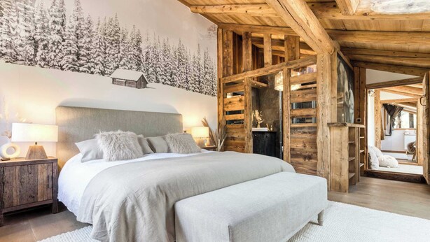 A bedroom with a large bed, wooden beams, a wall mural, and a cozy atmosphere.