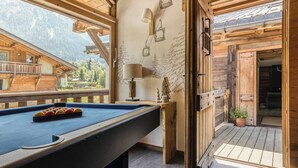 A pool table with balls, a lamp, and a ski lift mural in a wooden room with a view of mountains.