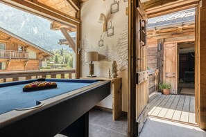 A pool table with balls, a lamp, and a ski lift mural in a wooden room with a view of mountains.