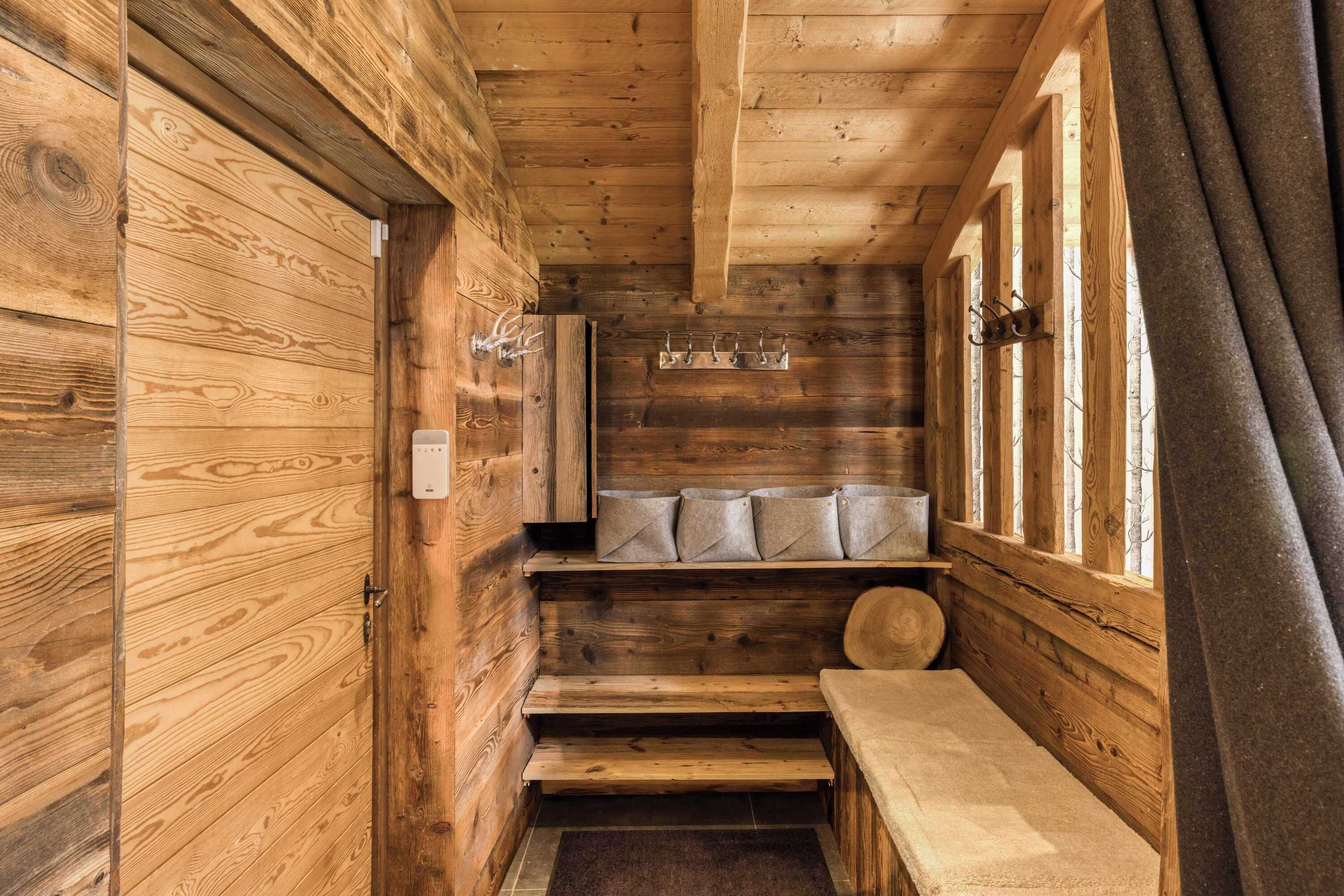 A wooden cabin interior with a bench, a coat rack, and a window with curtains.