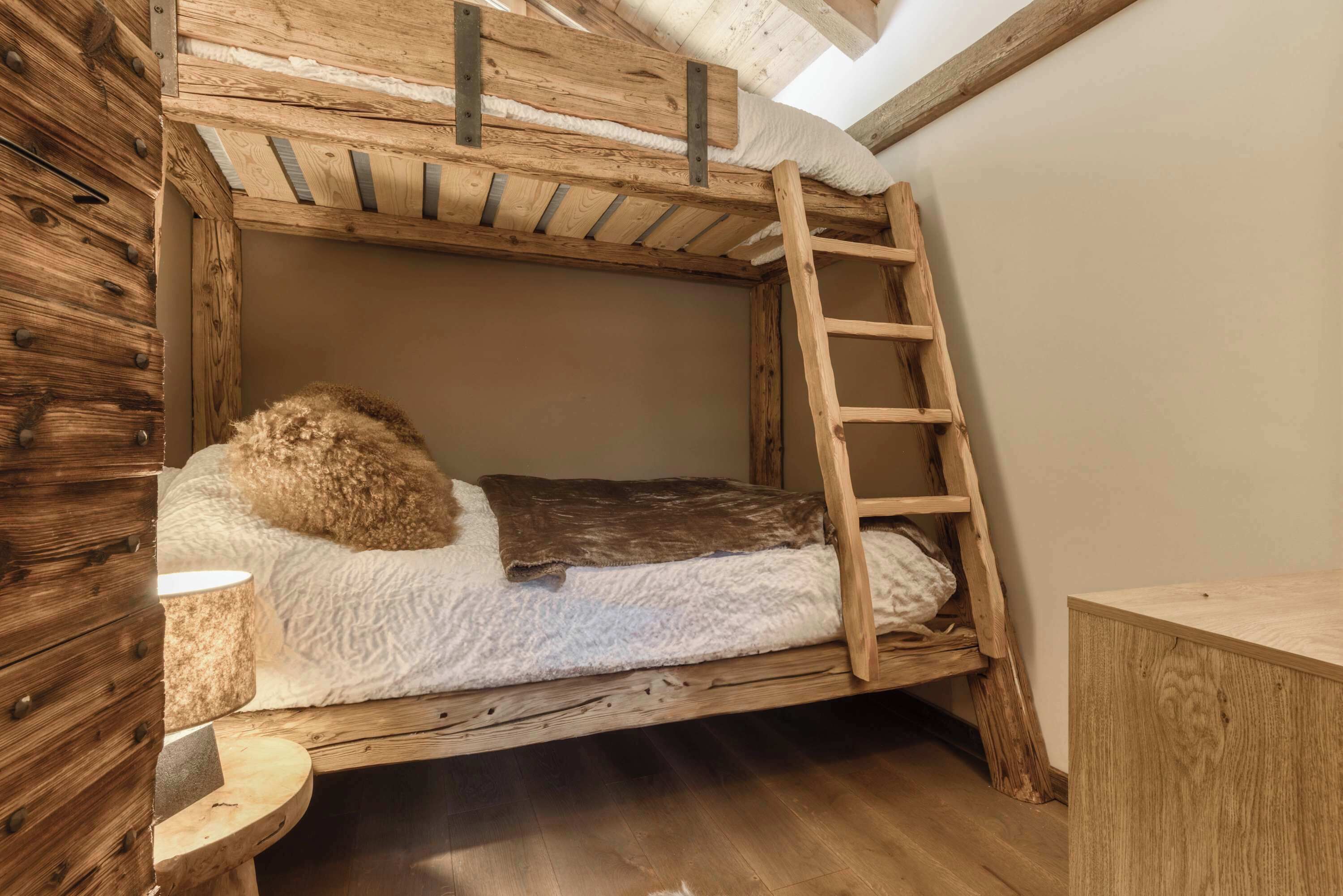 Un lit superposé avec une échelle, une commode en bois et une lampe.