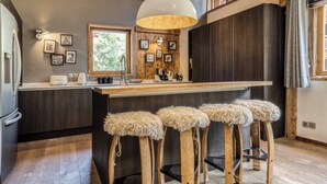 A modern kitchen with wooden stools, a large island, and a hanging light fixture.