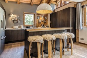 A modern kitchen with wooden stools, a large island, and a hanging light fixture.