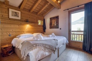 A wooden cabin bedroom with a bed, a window, and a door leading to a balcony. - Chalet Arte 12px Hot Bath Sauna (Les Houches)