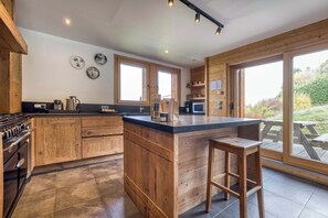 A kitchen with wooden cabinetry, a large island, and a view of the outdoors. - Chalet Arte 12px Hot Bath Sauna (Les Houches)