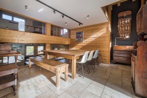 A spacious room with a wooden table and benches, a large window, and a view of the outdoors. - Chalet Arte 12px Hot Bath Sauna (Les Houches)