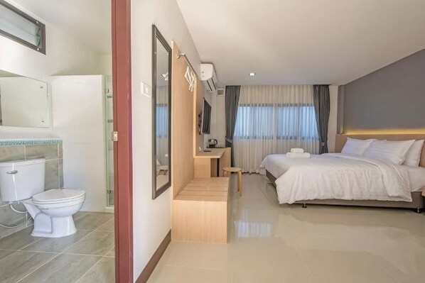 A hotel room with a bed, a bedside table, a mirror, a toilet, and a shower area. - Happiness Guesthouse (Pak Chong)