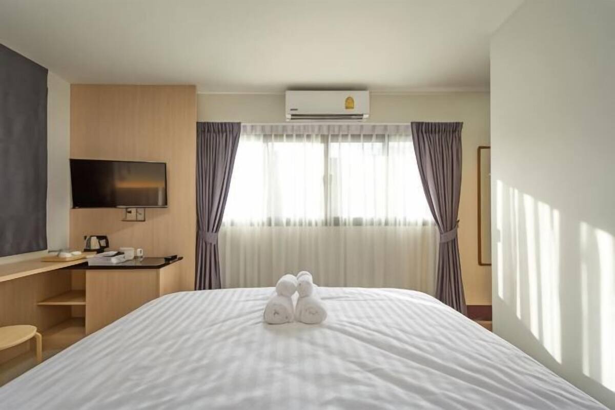A hotel room with a bed, a desk, a television, and an air conditioning unit.