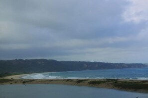 A coastal landscape with a beach, ocean, and hills in the distance. - Three Queen Villa and Homestay (Wanokaka)