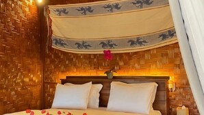 A bed with white bedding and a canopy, a wooden headboard, and a nightstand with a lamp. - Three Queen Villa and Homestay (Wanokaka)